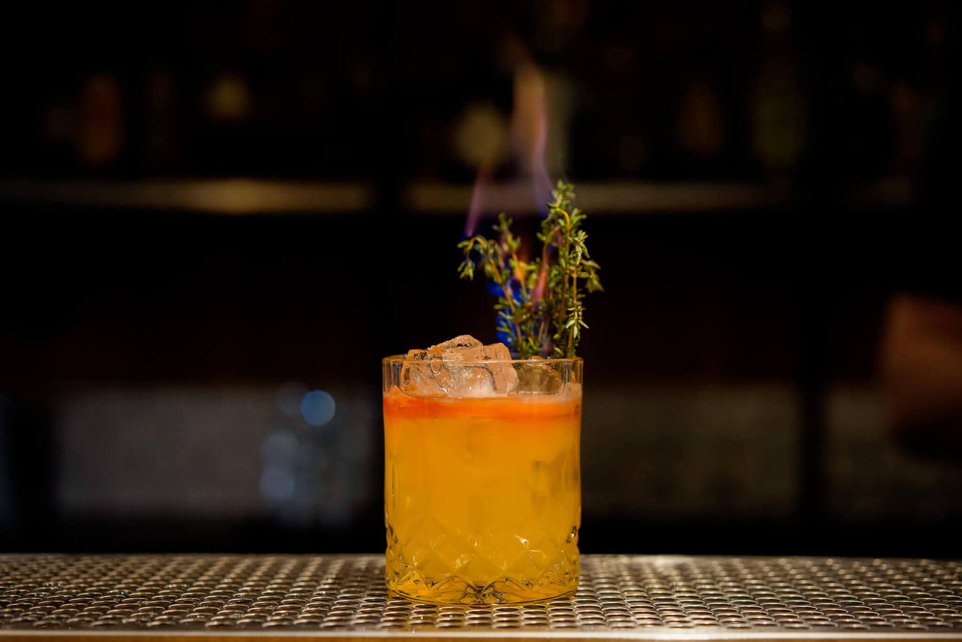 A flaming thyme-garnished craft cocktail on the bar at Cenote
